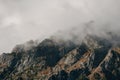 Dramatic fog among giant rocky mountains. Ghostly atmospheric view to big cliff in cloudy sky. Low clouds and beautiful rockies. Royalty Free Stock Photo