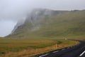 Dramatic iceland foggy landscape with a green hill and empty road.