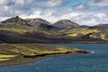 Dramatic iceland landscape with a green hill and black lava and and blue mirror mountain lake. Iceland