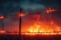 A dramatic image of a fire burning behind a barbed wire fence. Suitable for illustrating danger or destruction Royalty Free Stock Photo