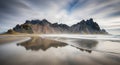 Dramatic mountain range reflected in a wet sandy beach with gentle waves and streaky clouds Royalty Free Stock Photo