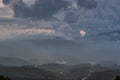 Dramatic landscape with gloomy blue rainy sky, heavy clouds and shining pink sunbeams after rain over smoky and hazy tropical.