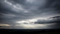 A dramatic landscape under a dark, stormy sky with rays of sunlight breaking through the heavy clouds, illuminating the distant Royalty Free Stock Photo
