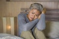 Dramatic lifestyle home portrait of attractive sad and lost middle aged woman with grey hair sitting on bed feeling frustrated