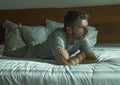 Dramatic lifestyle portrait of young attractive sad and depressed man lying on bed at home bedroom thoughtful and pensive feeling Royalty Free Stock Photo