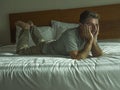 Dramatic lifestyle portrait of young attractive sad and depressed man lying on bed at home bedroom thoughtful and pensive feeling Royalty Free Stock Photo