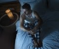 Dramatic lifestyle portrait of young attractive sad and depressed man sitting on bed at night feeling stressed and desperate