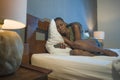 Dramatic lifestyle portrait of young sad and depressed black afro American woman crying in bed holding mobile phone victim of