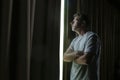 Dramatic light portrait of young sad and depressed attractive man at home looking through room window thoughtful and pensive lost Royalty Free Stock Photo