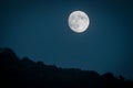 Dramatic mountain moon rise with deep blue night time sky and layered hills in the distance