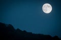 Dramatic mountain moon rise with deep blue night time sky and layered hills in the distance