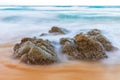 Dramatic moving wave around big rocks on clear water beach