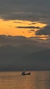 Dramatic orange and grey sunset over layered mountains. A lone ship sails on the reflective sea below Royalty Free Stock Photo