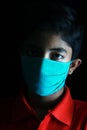 Dramatic portrait of a boy wearing medical face mask looking out deep in thought, Candid. Royalty Free Stock Photo