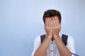 Dramatic portrait of desperate sad man on blue background. He is hiding his face