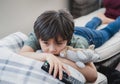 Dramatic portrait Lonely kid sad face holding remote control sitting on couch,child sitting on sofa in living room with looking Royalty Free Stock Photo