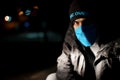 Dramatic portrait of a man in a blue protective mask during quarantine. Night street. Hard light. Coronavirus. Quarantine. Caption