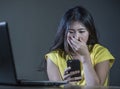 Dramatic portrait scared and stressed Asian Korean teen girl or young woman with laptop computer and mobile phone suffering cyber Royalty Free Stock Photo