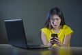 Dramatic portrait scared and stressed Asian Korean teen girl or young woman with laptop computer and mobile phone suffering cyber Royalty Free Stock Photo