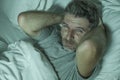 Dramatic portrait of stressed and frustrated man in bed awake at night suffering insomnia sleeping disorder tired and desperate