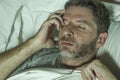 Dramatic portrait of stressed and frustrated man in bed awake at night suffering insomnia sleeping disorder tired and desperate