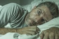 Dramatic portrait of stressed and frustrated man in bed awake at night suffering insomnia sleeping disorder tired and desperate