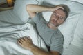 Dramatic portrait of stressed and frustrated man in bed awake at night suffering insomnia sleeping disorder tired and desperate