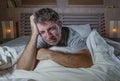 Dramatic portrait of young attractive sad and depressed man lying in bed crying desperate suffering depression problem and anxiety