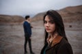 Dramatic portrait of a young brunette girl in cloudy weather. somewhere behind her, out of focus, her young lover boyfriend leaves