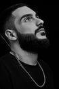 A dramatic portrait of a young serious guy, musician, singer, rapper with a beard in black clothes on a black isolated background