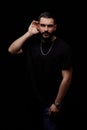 A dramatic portrait of a young serious guy, musician, singer, rapper with a beard in black clothes on a black isolated background