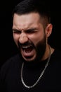 A dramatic portrait of a young serious guy, musician, singer, rapper with a beard in black clothes on a black isolated background