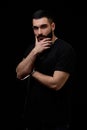 A dramatic portrait of a young serious guy, musician, singer, rapper with a beard in black clothes on a black isolated background