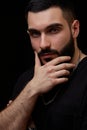 A dramatic portrait of a young serious guy, musician, singer, rapper with a beard in black clothes on a black isolated background