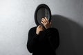 Dramatic portrait of young thoughtful guy, looking at his reflection in black oval mirror on textured wall of grey color.