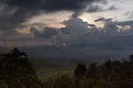 Dramatic rainy dark sky on sunset - heavy blue clouds and shining orange, yellow sunbeams after rain over smoky tropical valley. Royalty Free Stock Photo