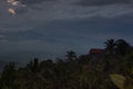 Dramatic rainy Indonesian landscape with gloomy dark blue- grey sky over hazy tropical green valley with forest, mountains, rural