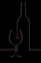 A dramatic rim light outlines a bottle and glass of red wine Royalty Free Stock Photo