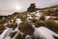 A dramatic rocky mountain landscape with snow and grass in the foreground