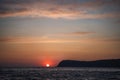 Dramatic Seascape over black sea surface during sunset, Silhouette of rocky volcanic cliff is lit by the warm sunset Royalty Free Stock Photo