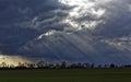 Sun rays through dark clouds over a field and shower in the background Royalty Free Stock Photo