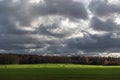 Dramatic sky with dark rain clouds over green agricultural field with tractor tracks in autumn landscape Royalty Free Stock Photo