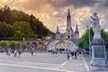 Dramatic sky on the esplanade of the Rosary Basilica with the crowd of pilgrims at Lourdes, France.