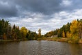 Dramatic sky with gray dark clouds on cloudy autumn day. Fall season beautiful view of small lake or pond surrounded by colorful Royalty Free Stock Photo