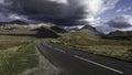 Dramatic sky over country road leading to mountain range in background Royalty Free Stock Photo