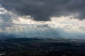 Dramatic sky with sun rays breaking through heavy clouds over a rural landscape, illuminating fields and villages below. Royalty Free Stock Photo