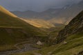 Dramatic sky with thunderstorm weather in summer mountains - gorge with green hilly slopes in golden sunlight with road