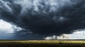 A dramatic storm cloud looms over a vast grassy plain, casting a dark shadow and threatening rain Royalty Free Stock Photo