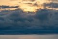 Dramatic storm clouds above sea water surface with golden sunrise behind the clouds on a warm day of early autumn. Royalty Free Stock Photo