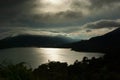 Dramatic storm in mountains landscape - heavy rain fluffy clouds and sunbeams over black mountains and bright shine lake. Royalty Free Stock Photo